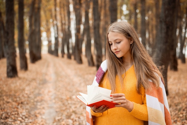 Hermosa chica rubia con un libro en sus manos en un parque de otoño