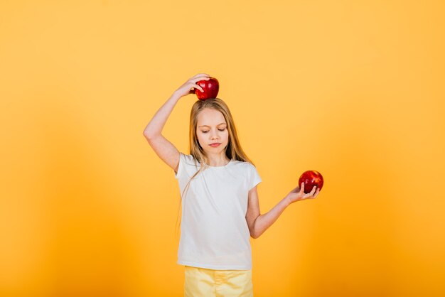 Hermosa chica rubia con manzana roja en estudio, fondo amarillo