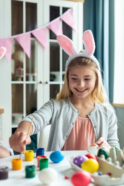 Hermosa chica rubia en orejas de conejo para colorear huevos, feliz Pascua