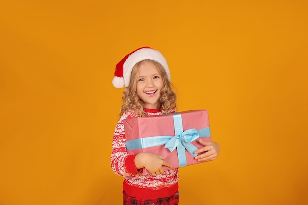 una hermosa chica rubia en un puente de Navidad gorro de Papá Noel tiene una caja de regalo