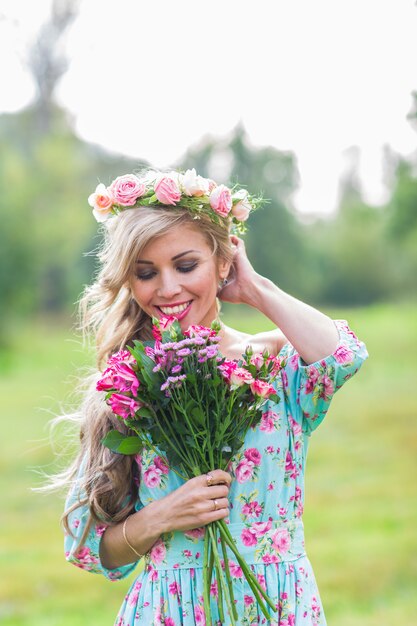 Hermosa chica rubia con ramo de flores en el campo.