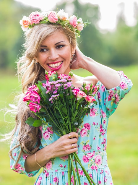 Hermosa chica rubia con ramo de flores en el campo.