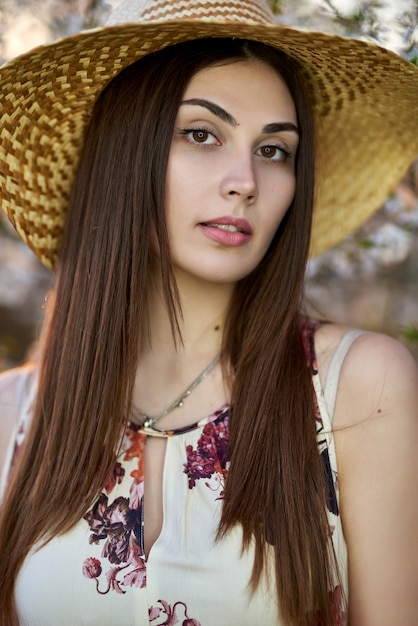 Hermosa chica rubia con un ramo de ramas con flores en un sombrero de paja y un vestido en un jardín de primavera donde florecen los árboles