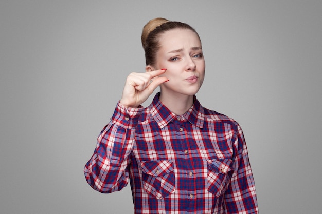 Hermosa chica rubia en rojo, camisa a cuadros rosa, peinado de moño recogido, maquillaje de pie y mirando a la cámara y rogando por algunas cosas más. tiro de estudio interior. aislado sobre fondo gris