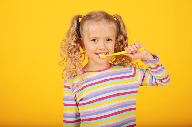 una hermosa chica rubia sobre un fondo amarillo en una chaqueta de color con un cepillo de dientes