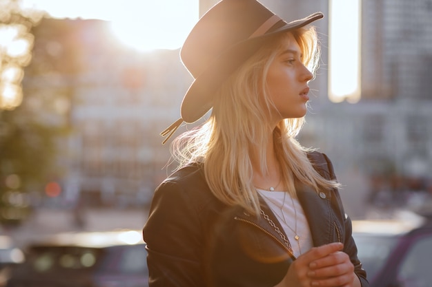 Hermosa chica rubia con sombrero negro posando con la cálida luz del sol. Espacio para texto