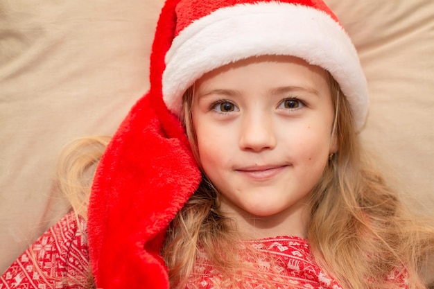 una hermosa chica rubia con un sombrero de Santa Claus y pijamas de Año Nuevo está durmiendo en la cama