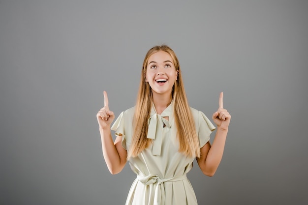 Hermosa chica rubia sonriente apuntando hacia arriba en copyspace aislado