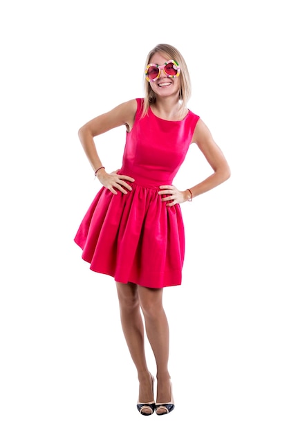 Hermosa chica rubia sonriente en un vestido rojo romántico gafas divertidas y tacones altos Positividad y alegría Aislado sobre fondo blanco Vertical