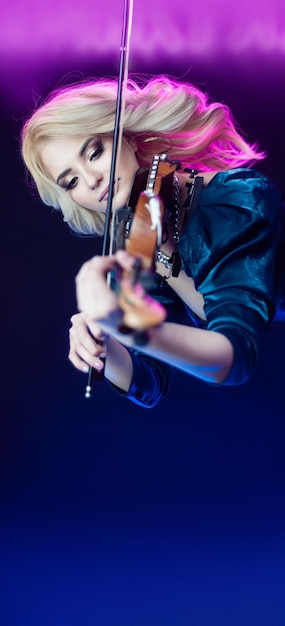 Hermosa chica rubia tocando el violín con luz de neón en el fondo
