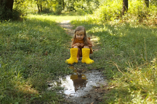 una hermosa chica rubia con un traje de lino color mostaza vierte agua de una bota amarilla