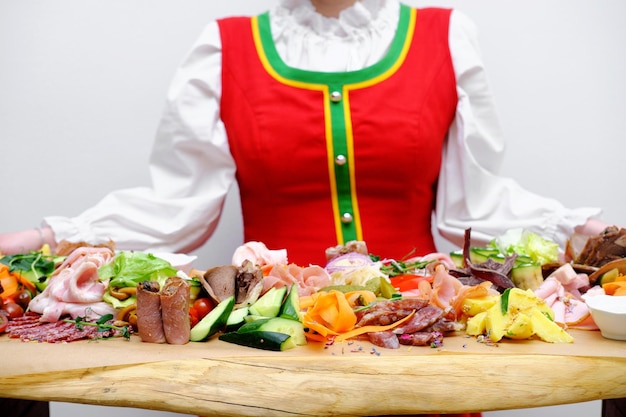 Hermosa chica rusa sonriente en traje folklórico se encuentra cerca de la mesa del buffet y ofrece bocadillos