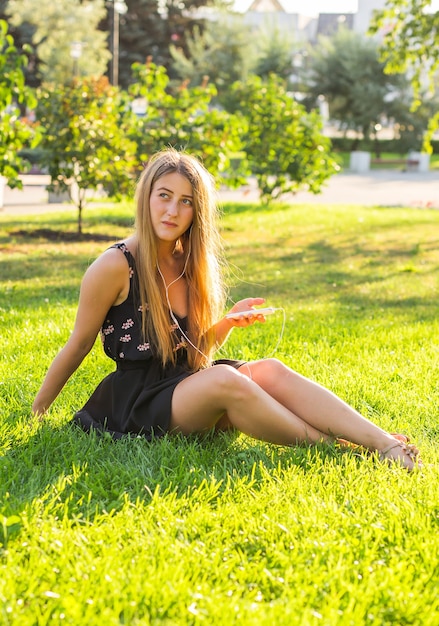 Hermosa chica sentada en el césped del parque y escuchar música.