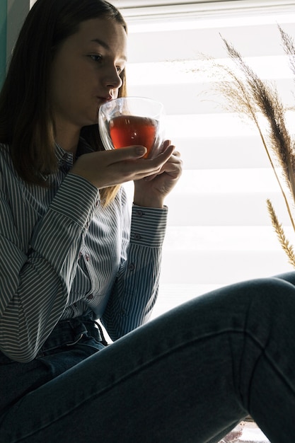 Hermosa chica sentada con una expresión pensativa en su rostro sosteniendo una taza de té