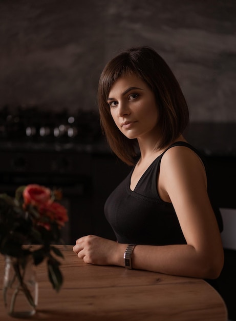 Hermosa chica sentada en una mesa en una cocina oscura