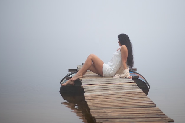 Hermosa chica sentada en el muelle junto al río