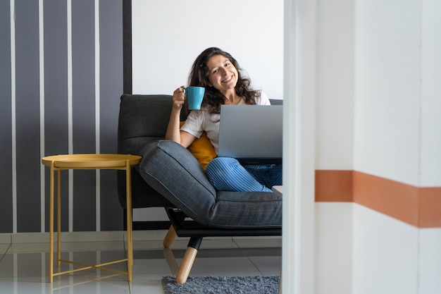 Hermosa chica sentada con un ordenador portátil en un sofá en una habitación elegante. Trabajar desde casa. Ambiente de trabajo de buen humor.