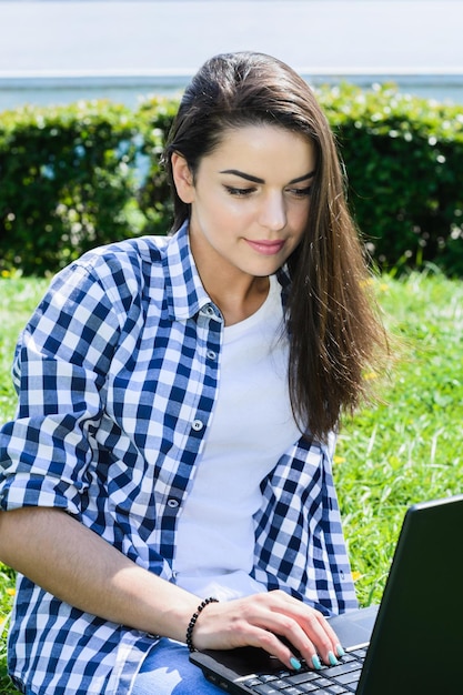 Hermosa chica sentada en el parque con una laptop