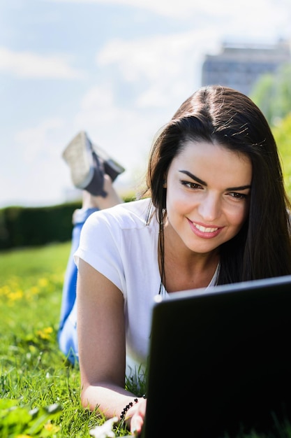 Hermosa chica sentada en el parque con una laptop