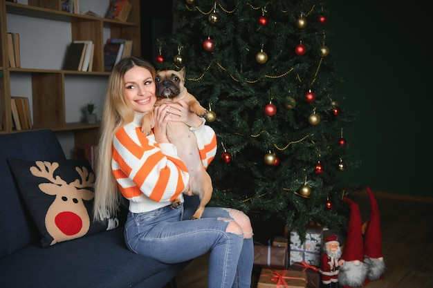 Hermosa chica sentada en el sofá con un perro en el fondo de Navidad