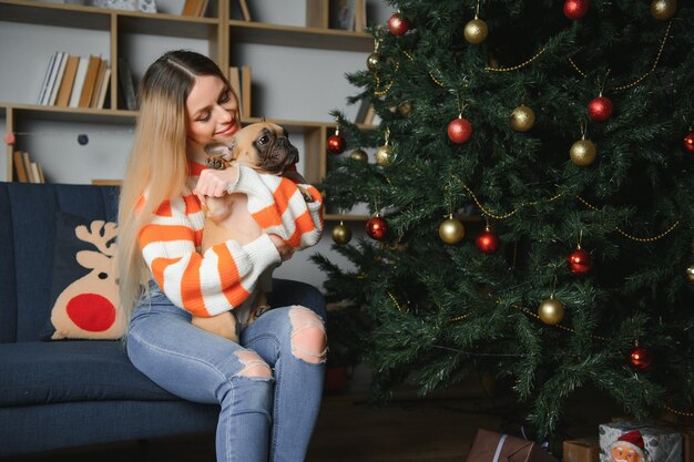 Hermosa chica sentada en el sofá con un perro en el fondo de Navidad