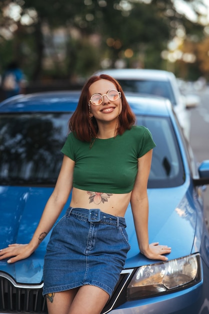 Hermosa chica se sienta en el capó de un coche azul