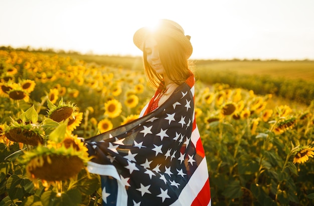 Hermosa chica con sombrero con bandera estadounidense en un campo de girasoles 4 de julio Día de la Independencia