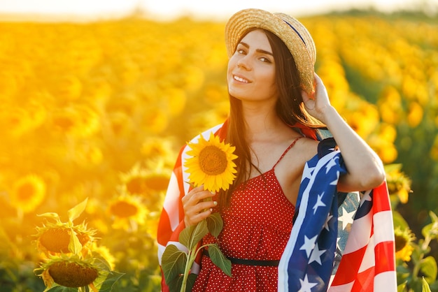 Hermosa chica con sombrero con la bandera estadounidense en un campo de girasoles 4 de julio Libertad del 4 de julio