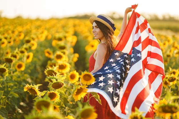 Hermosa chica con sombrero con la bandera estadounidense en un campo de girasoles 4 de julio Libertad del 4 de julio