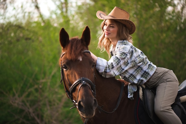 Hermosa chica con un sombrero a caballo en el campo