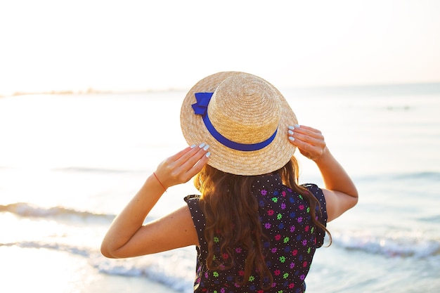 Hermosa chica en un sombrero se encuentra de espaldas en la playa de arena