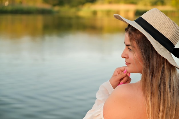 Una hermosa chica con un sombrero se encuentra en la orilla con el sombrero en la mano.