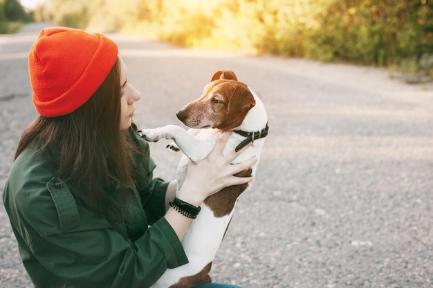 Una hermosa chica con un sombrero naranja sostiene a su perro en sus brazos la chica cuida a su mascota