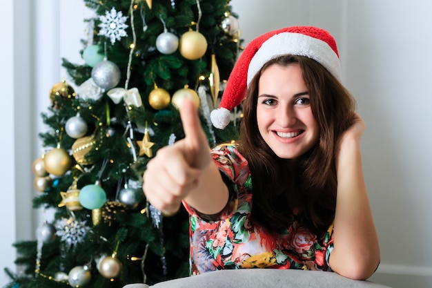 Hermosa chica con un sombrero de Navidad mostrando Thumbs up sign OK