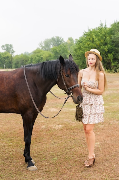 Hermosa chica con sombrero de paja y vestido de verano con un caballo