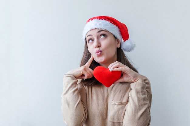 Hermosa chica con sombrero rojo de Santa Claus con corazón rojo en la mano aislado sobre fondo blanco.