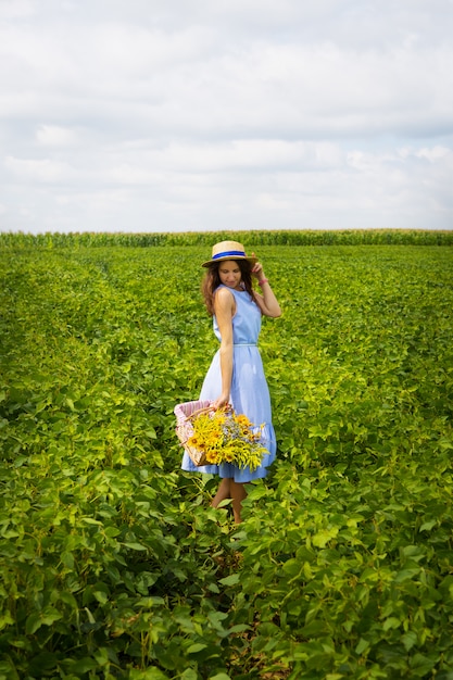 Hermosa chica en un sombrero y tablero azul está de pie sobre un campo verde