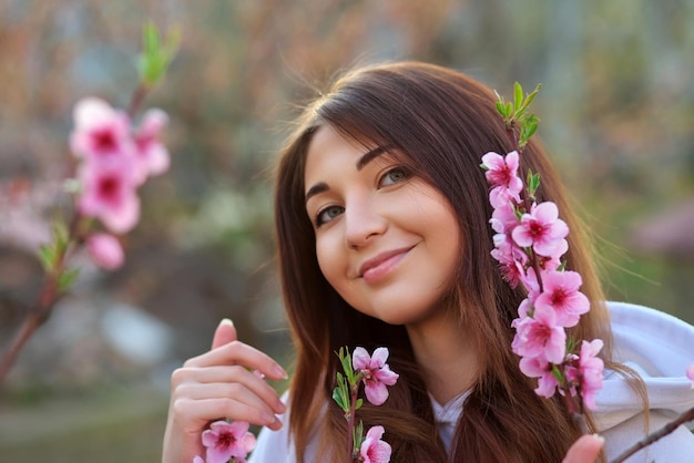 Hermosa chica sonriente de pie cerca de un árbol de durazno durante la puesta de sol Cara feliz Tiempo de primavera