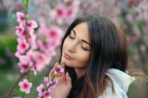 Hermosa chica sonriente de pie cerca de un árbol de durazno durante la puesta de sol Cara feliz Tiempo de primavera