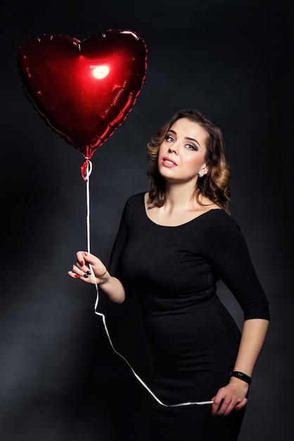 Hermosa chica sosteniendo un gran globo rojo en forma de corazones en el Día de San Valentín