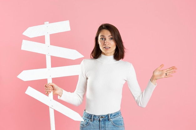 Foto hermosa chica sosteniendo señales de tráfico blancas en su mano aisladas en un fondo rosa