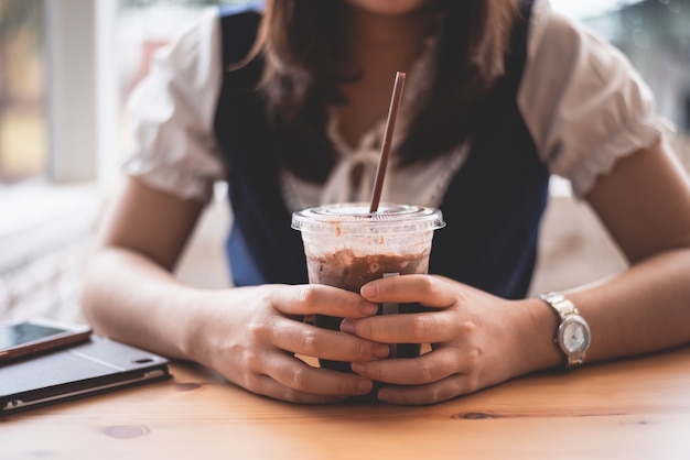 Hermosa chica sosteniendo una taza de café con hielo en el café