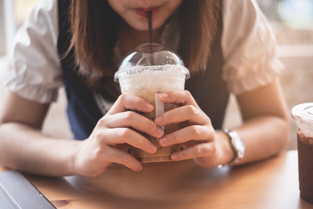 Hermosa chica sosteniendo una taza de café con hielo en el café