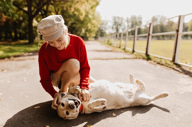 Hermosa chica con su perro pasando un gran día juntos en el parque Elegante rubia y su labrador relajándose bajo el sol en otoño