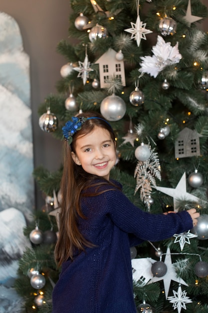 Hermosa chica con un suéter azul decora el árbol de Navidad en casa