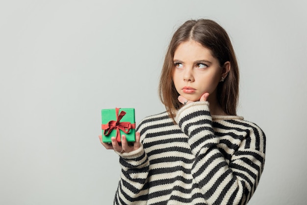 Hermosa chica en suéter de rayas con caja de regalo sobre fondo blanco.