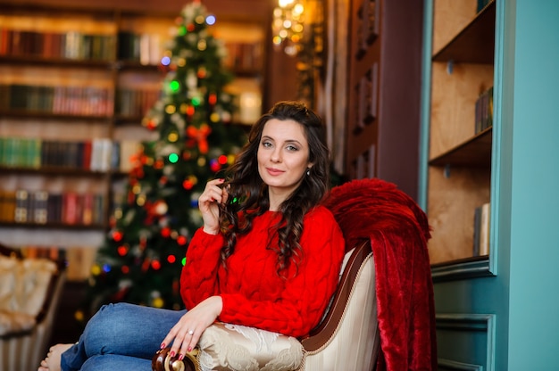 Hermosa chica con un suéter rojo cerca del árbol de Navidad.