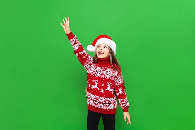 Una hermosa chica en un suéter rojo con renos alcanza tu anuncio en un fondo verde aislado El concepto de Navidad