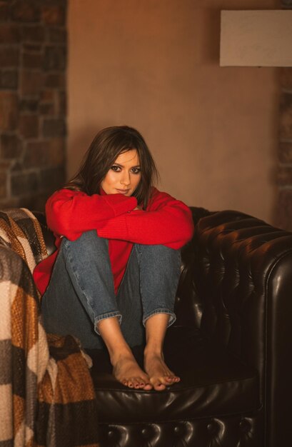 Foto una hermosa chica con un suéter rojo está sentada en un acogedor sillón y sonriendo