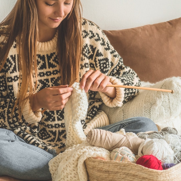 Hermosa chica teje un suéter caliente en la cama. Tejer como hobby. Accesorios para tejer.